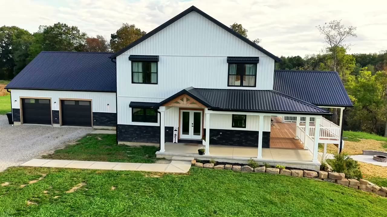 Cinematic aerial orbit of a modern farmhouse with a covered porch and black metal roof, filmed by Horizon Heights Productions.