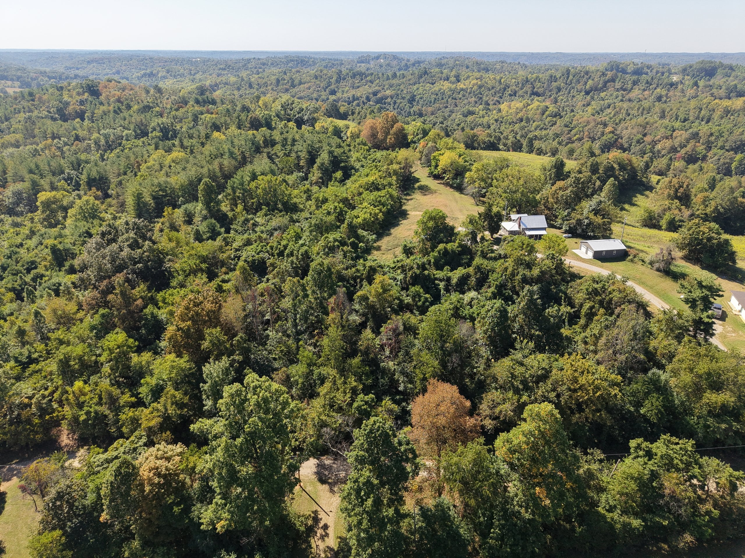 Aerial drone photograph over rolling wooded hills and a hilltop homestead in the Mid-Ohio Valley, captured by Horizon Heights Productions.